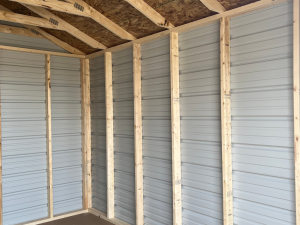 Close-up of interior of a small shed with exposed wooden framing, metal panel walls, and oriented strand board on the roof
